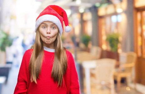 年轻漂亮的女孩戴着圣诞帽在孤立的背景上，使鱼的脸与嘴唇疯狂和滑稽的姿态。 有趣的表情。