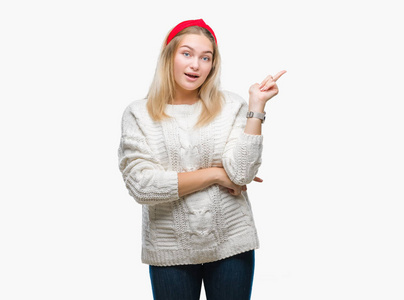 年轻的高加索女人穿着冬天的毛衣，在孤立的背景上，脸上挂着一个大大的微笑，用手和手指指向一边，看着相机。