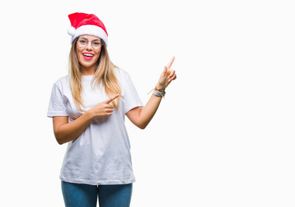 年轻漂亮的女人戴着圣诞帽，在孤立的背景上微笑着，看着相机，两只手和手指指向一边。