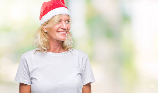 中年金发女人戴着圣诞帽，在孤立的背景上看着一边，脸上带着微笑，自然的表情。 自信地笑着。