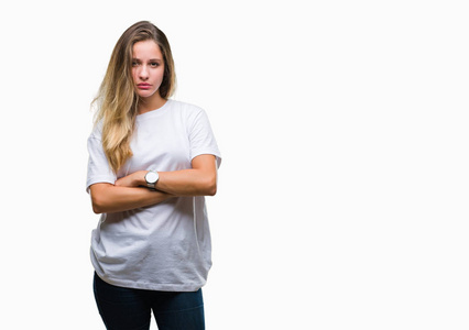 年轻漂亮的金发女人穿着休闲的白色T恤，在孤立的背景怀疑和紧张的不赞成的表情在脸上交叉的手臂。 消极的人。