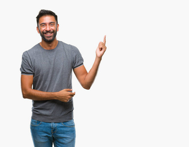 成年西班牙裔男子在孤立的背景上，脸上挂着一个大大的微笑，用手和手指指向一边，看着相机。