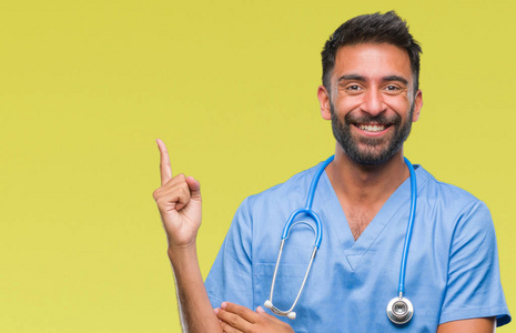 成年西班牙裔医生或外科医生，男人在孤立的背景上，脸上有一个大大的微笑，用手和手指指向一边，看着相机。