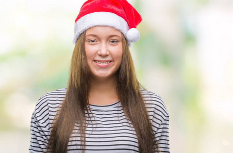 年轻美丽的高加索女人戴着圣诞帽，在孤立的背景上，脸上带着快乐和凉爽的微笑。 幸运的人。