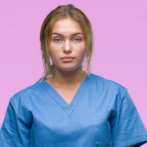 年轻的白种人护士女士穿着外科医生制服，在孤立的背景上，脸上有严重的表情。 简单自然地看着相机。