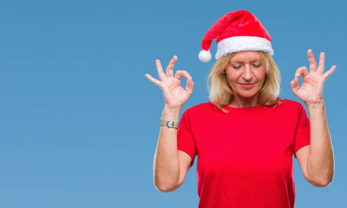 中年金发女人戴着圣诞帽，戴着孤立的背景，放松，闭着眼睛微笑，用手指做冥想手势。 瑜伽概念。
