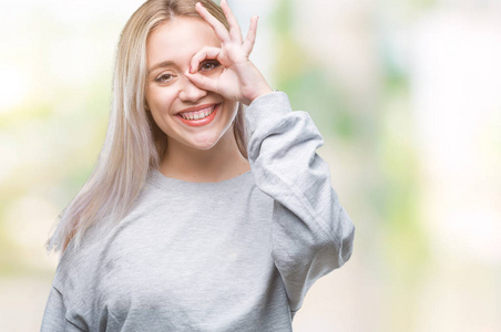 年轻的金发女人在孤立的背景下做好手势，用手微笑的眼睛透过手指看着快乐的脸。