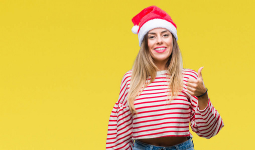 年轻漂亮的女人戴着圣诞帽，在孤立的背景上，用手做快乐的竖起大拇指的手势。 赞许的表情看着相机，显示出成功。