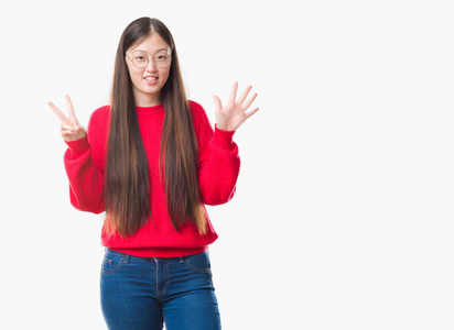 年轻的中国女人在孤立的背景下，戴着眼镜，用手指七号，微笑着自信和快乐。