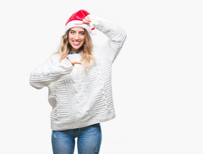 美丽的年轻金发女人戴着圣诞帽，在孤立的背景上微笑，用手和手指制作框架，用快乐的脸。 创造力和摄影理念。
