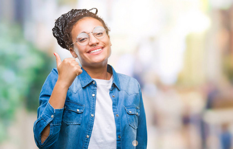 年轻的辫子非裔美国女孩戴着眼镜，在孤立的背景下，用手做快乐的竖起大拇指的手势。 赞许的表情看着相机，显示出成功。