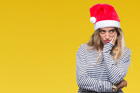 美丽的年轻金发女人戴着圣诞帽，在孤立的背景下，认为穿着交叉的手臂看起来很累，厌倦了抑郁的问题。