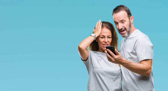 中年西班牙裔夫妇在智能手机上发短信，在孤立的背景下，用手压在头上，羞愧和惊讶的脸，愤怒和沮丧。 因为错误而恐惧和不安。