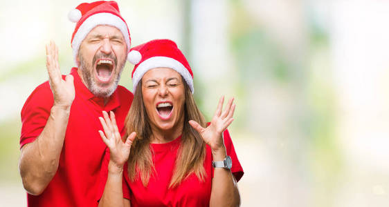 中年西班牙裔夫妇戴着圣诞帽，在孤立的背景下庆祝疯狂和疯狂的成功，举起双臂，闭上眼睛，尖叫兴奋。 赢家概念