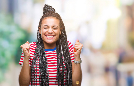 年轻的辫子非洲裔美国女孩在孤立的背景下兴奋地成功，举起双臂庆祝胜利，微笑。 赢家概念。