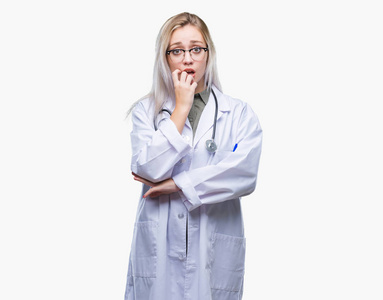 年轻的金发医生女人在孤立的背景上看着压力和紧张，双手咬着嘴的指甲。 焦虑问题。