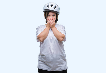 年轻的成年骑自行车的妇女患有唐氏综合症，戴着安全帽，在孤立的背景下震惊地用手捂住嘴，因为错误。 秘密概念。