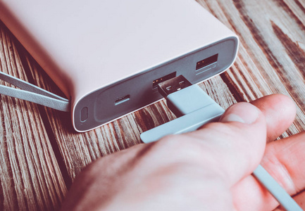 一只手将USB电缆连接到木制背景上的电源库。 外部电池。