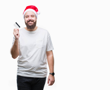 年轻的白种人戴着圣诞帽，背着信用卡，脸上挂着幸福的笑容，露出自信的牙齿