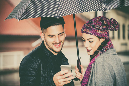 幸福的一对年轻人和一个带着雨伞的女人在城里用手机