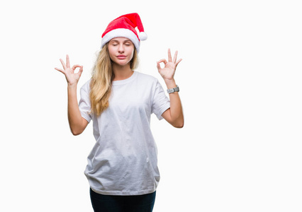年轻漂亮的金发女人戴着圣诞帽，在孤立的背景上放松，闭着眼睛微笑，用手指做冥想手势。 瑜伽概念。