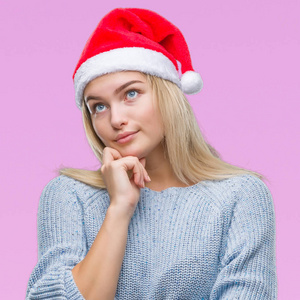 年轻的高加索女人戴着圣诞帽，戴着孤立的背景，手拿着下巴，思考着问题，沉思的表情。 带着体贴的脸微笑。 怀疑概念。