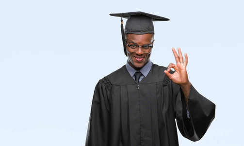 年轻毕业的非裔美国人，在孤立的背景下微笑，积极地做好手和手指的OK标志。 成功的表达。