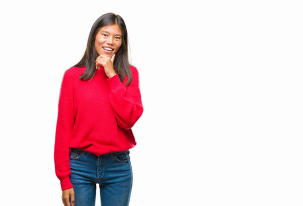 年轻的亚洲女人穿着冬天的毛衣，在孤立的背景下，自信地看着相机，微笑着交叉的手臂和举起的手在下巴上。 积极思考。