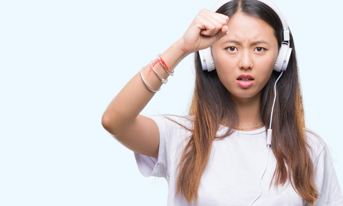 年轻的亚洲女人，听音乐，戴着耳机，背景，烦恼和沮丧，愤怒，疯狂地大喊大叫，举起手愤怒的概念