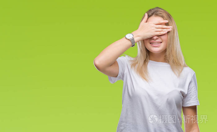 年轻的白种人女人在孤立的背景上微笑和笑用手捂着眼睛以获得惊喜盲目