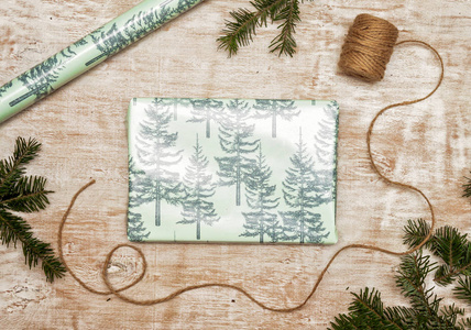 包装新年和圣诞礼物的过程，一支云杉绳，绿色和粉红色的纸在木制背景上。 顶部视图复制空间平躺。