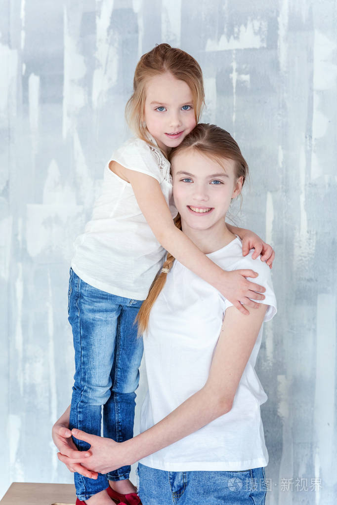 两个快乐的孩子站在灰色纹理的墙壁背景和拥抱.