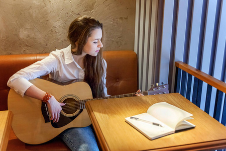 年轻微笑的时髦女人坐在咖啡馆里弹吉他，写一首歌。女孩学习演奏音乐