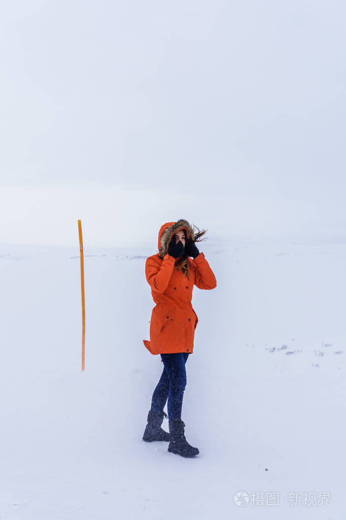 一个穿着鲜艳橙色夹克的女孩在冬天寒冷的冬天在冻土带的暴风雪中徒步