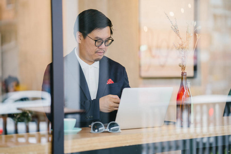 一个穿着马球和夹克的中国人白天坐在咖啡馆里用笔记本电脑工作的肖像。