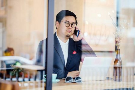 山羊坐一个穿着马球和夹克的中国人白天坐在咖啡馆里用笔记本电脑工作