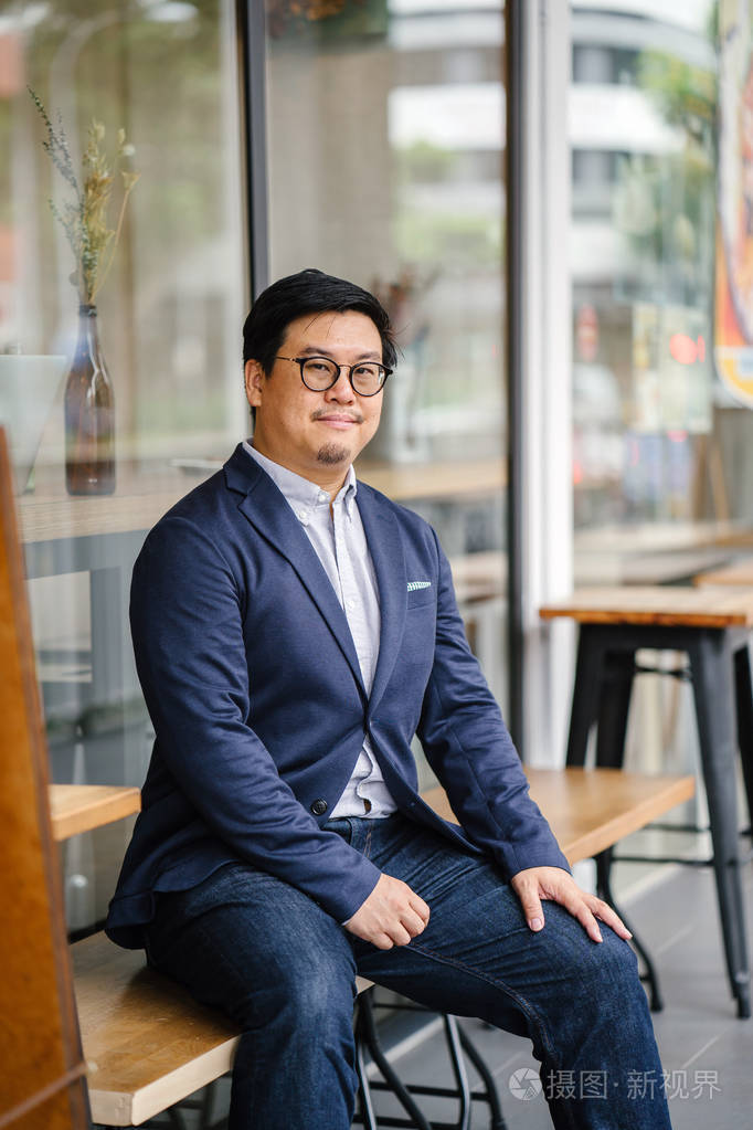 中年中国亚裔男子的肖像牛津衬衫夹克和牛仔裤的纽扣他戴着眼镜看上去