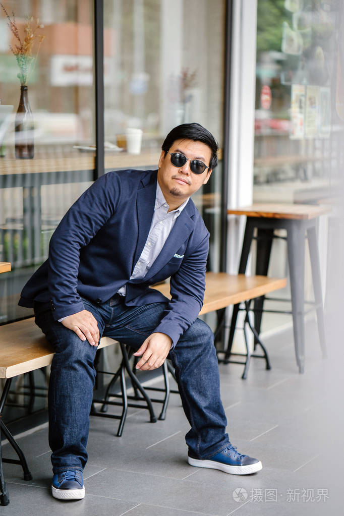 中年中国亚裔男子的肖像牛津衬衫夹克和牛仔裤的纽扣他戴着眼镜看上去