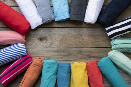 把卷好的五颜六色的衣服放在木制桌子的背景上,做成圆形照片