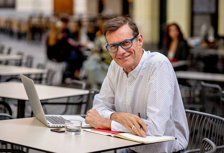 开朗微笑的老人在电脑上工作，在户外露台咖啡店喝咖啡，在老年人中使用现代技术保持联系和企业家创意商业理念。
