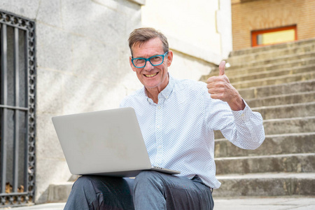 时尚的老人在笔记本电脑上工作，上网，坐在户外城市的楼梯上，在数字游牧中，老年人使用现代技术保持联系和企业家创意的商业理念。