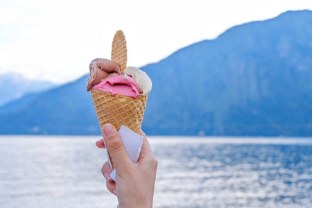 女人手拿着华夫饼冰淇淋。 科莫湖和山脉背景在日落。 意大利