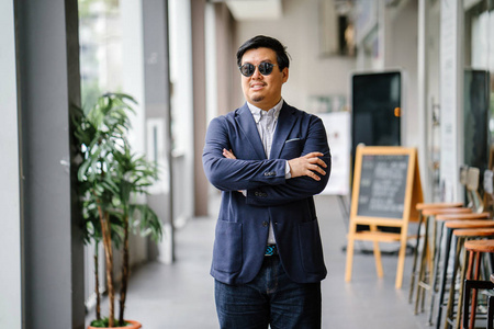 一位中年中国亚裔男子新加坡人的肖像，穿着智能休闲，站在城市里。 他穿着考究，穿着一件海军服，牛津纽扣，衬衫上戴着太阳镜。