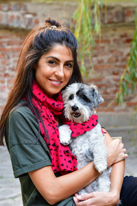 美丽的微笑的女人用红领巾拥抱她可爱的哈万尼犬。主人和狗的时尚。