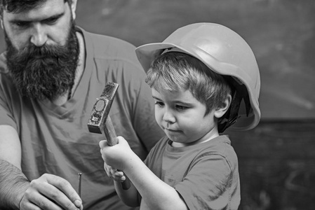 男孩, 孩子忙着保护头盔学习用锤子和爸爸在一起。父亲的概念。父亲用胡子教小儿子使用工具, 锤击, 黑板在背景上