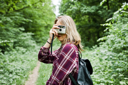一个穿格子衬衫的漂亮年轻女孩的肖像，在森林里用相机拍照。