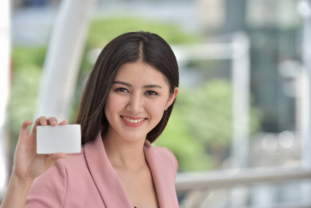 穿着粉红色西装的亚洲女孩把甜蜜的微笑送到一只手拿着信用卡的手上。 漂亮的女商人，穿着苹果平板电脑。 用来检查电子邮件和表达喜悦时