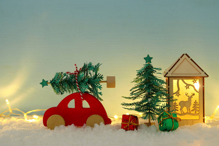 蓝色背景和金色花环灯光前，红色的木车载着一棵圣诞树在雪地上