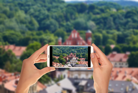 一位游客正在用手机拍摄维尔纽斯全景照片，观看圣弗朗西斯阿西西教堂