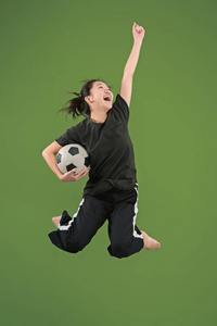 走向胜利。年轻女子作为足球运动员跳跃和踢球在工作室绿色